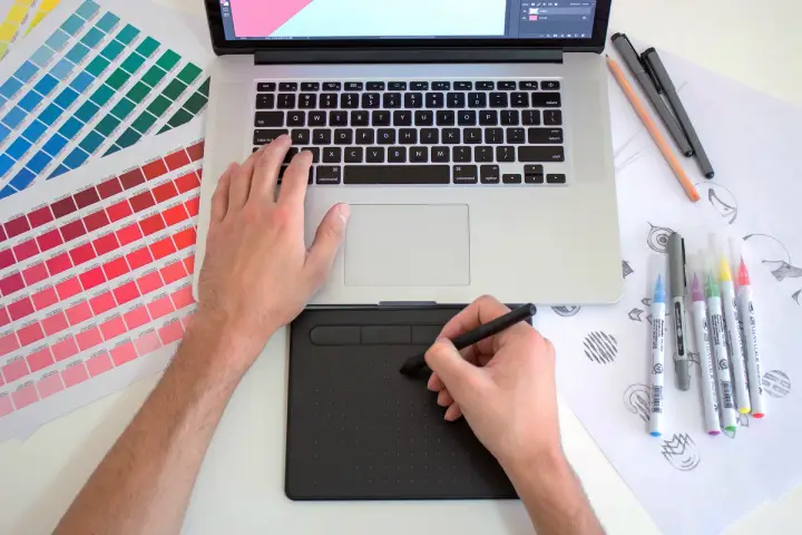 A designer using a graphic tablet, with colour charts, logo designs and marker pens
